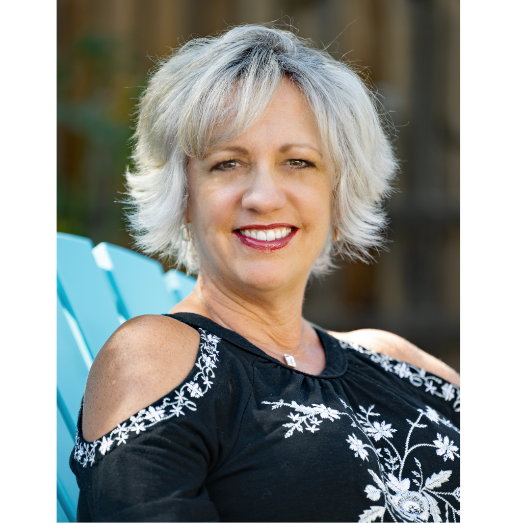Jena Taylor, resiliency coach wearing black shoulder-open shirt with white embroidery smiling on a turquoise chair.
